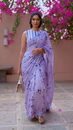 Indian woman in Neerja lavender bloom linen saree — full length frontal, bougainvillea backdrop, cobalt-striped blouse, scalloped hem, soft daylight